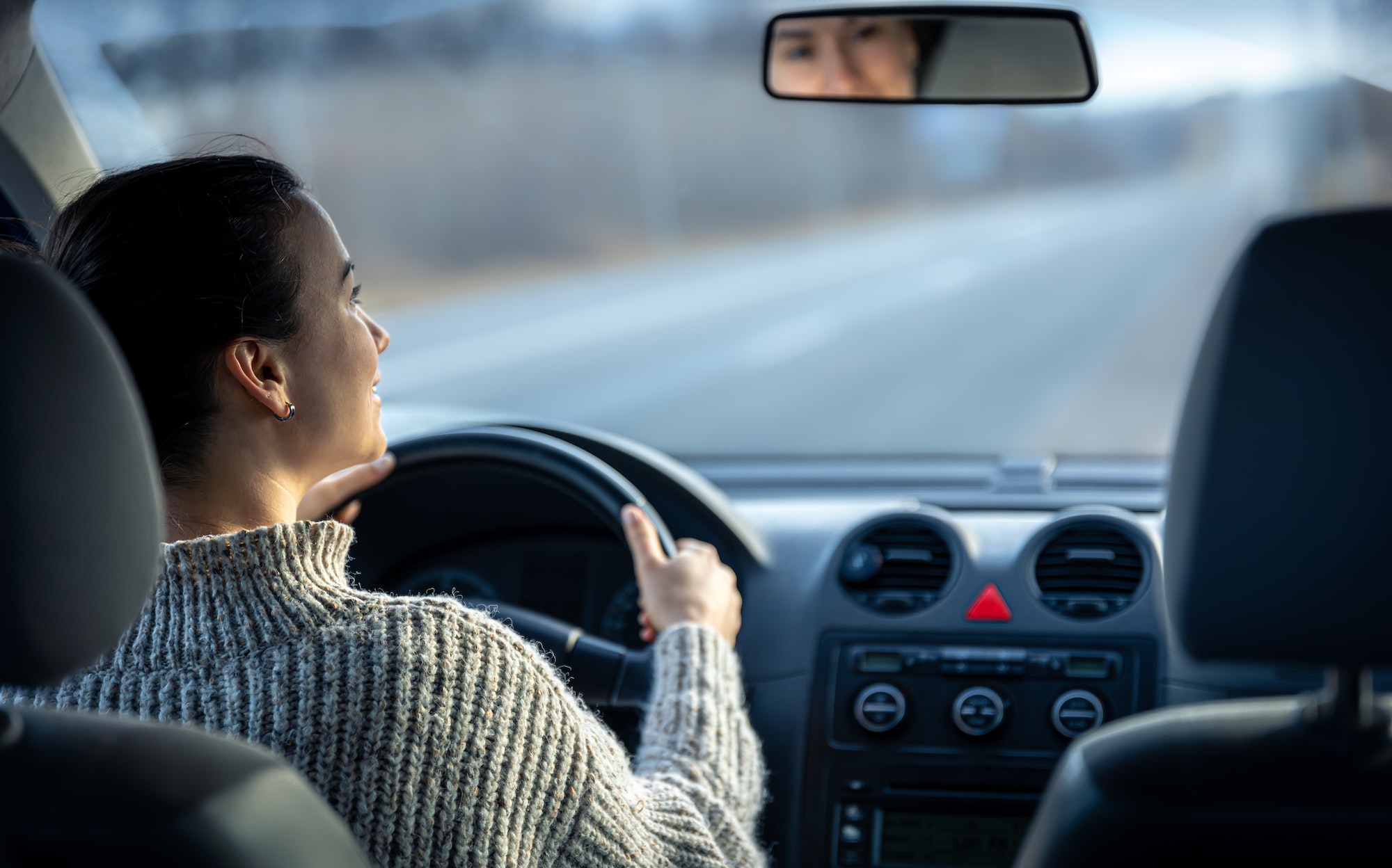 Happy young woman drives a car, inside view.